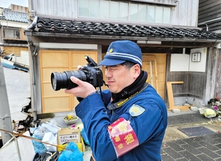 能登半島地震の被災地に記録係として派遣された兵庫県警警部補の葛西智広さん。一変した故郷の町でカメラを構える＝２月９日、石川県輪島市（県警提供）