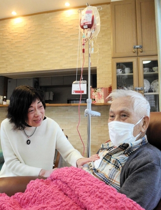 自宅で輸血を受ける村瀬成一さん（右）を妻の清子さんが見守る＝西宮市内