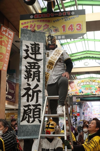 マジックナンバー「１４３」のボードの前で連覇を祈願する商店街関係者＝２７日午前、尼崎市神田中通３