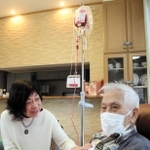 自宅で輸血を受ける村瀬成一さん（右）を妻の清子さんが見守る＝西宮市内
