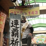 マジックナンバー「１４３」のボードの前で連覇を祈願する商店街関係者＝２７日午前、尼崎市神田中通３