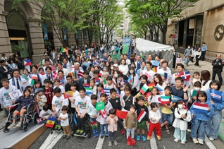 開幕２０日前イベントで万国旗を手に記念写真を撮る参加者＝２７日午後、神戸市中央区明石町（撮影・小林良多）