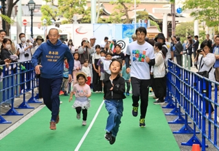 開幕２０日前イベントで開かれた走り方教室で北京五輪銀メダリストの朝原宣治さんと走る参加者＝２７日午後、神戸市中央区明石町（撮影・小林良多）