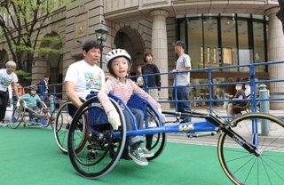 開幕２０日前イベントで競技用車いすを体験する子どもら。中央はアテネパラ銅メダリストの永尾嘉章さん＝２７日午後、神戸市中央区明石町（撮影・小林良多）