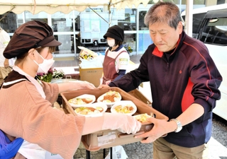 炊き出しのカレーライスを「神戸・心絆」のメンバー（左）から受け取る避難者