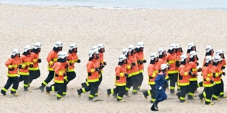 初夏の砂浜で、防火衣を着て走る消防学校の学生たち＝神戸市須磨区若宮町１