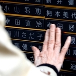 阪神・淡路大震災の４日後に亡くなった父親・幸田直治さんと母親・好子さんの銘板をなでる雅子さん＝神戸市中央区加納町６、東遊園地（撮影・長嶺麻子）