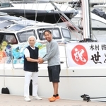 ミランダ号の前で堀江謙一さん（左）と握手する木村啓嗣さん＝９日午前、西宮市西宮浜４、新西宮ヨットハーバー（撮影・吉田敦史）