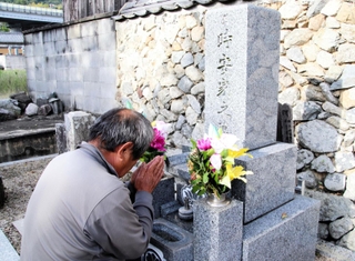 台風23号で亡くなった父孝行さんの墓前で手を合わせる正明さん＝洲本市上内膳