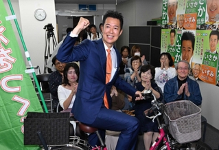 選挙区の遊説で使用した自転車にまたがり、ガッツポーズを見せる井坂信彦氏＝神戸市中央区八幡通４（撮影・風斗雅博）