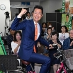 選挙区の遊説で使用した自転車にまたがり、ガッツポーズを見せる井坂信彦氏＝神戸市中央区八幡通４（撮影・風斗雅博）