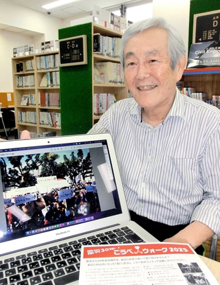 第１回の「こうべあいウォーク」の写真と次回のチラシを前に語る実行委員長の野崎隆一さん＝神戸市中央区