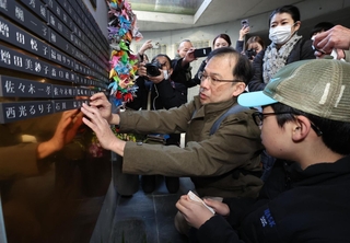 姉と両親の銘板を取り付ける兒玉隆之さん（中央）＝１４日午後、神戸市中央区加納町６、東遊園地（撮影・笠原次郎）