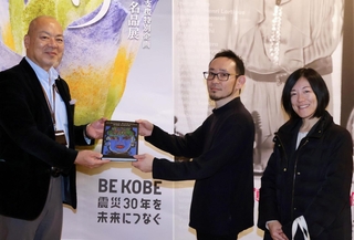石井嘉彦副館長（左）から記念品を受けとる石野慎一郎さん（中央）、真冬さん夫婦＝神戸ファッション美術館