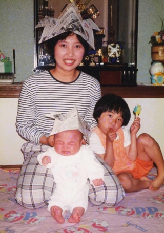 新聞紙で作ったかぶとをかぶって笑顔を見せる羽中幸恵さんと、ぴったりくっつく愛梨ちゃん（右）。敬登ちゃんは泣き顔だ＝１９９４年（羽中健二さん提供）