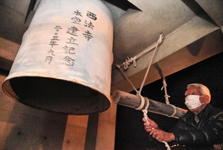 震災を語り継ぐためにつるされたドラム缶の鐘を鳴らす参列者＝芦屋市茶屋之町、西法寺