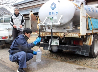 給水車から水をくみ住民に提供する市川町職員（手前）＝市川町鶴居、鶴居公民館