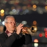 夜明け前の街明かりを背に、トランペットで鎮魂の音色を奏でる松平晃さん＝２０２４年１月１７日午前５時４６分、神戸市中央区神戸港地方（撮影・小林良多）