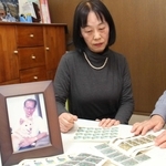 父裕さんの遺影を前に、父が集めていた切手を眺める石田優子さん（中央）と祥子さん（右）。祥子さんは顔の撮影を固辞した＝明石市内
