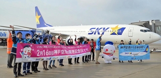 開港記念日を祝う横断幕を掲げ、搭乗客に手を振る航空会社の社員ら＝１６日午前、神戸空港（撮影・風斗雅博）