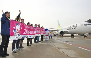 開港記念日を祝う横断幕を掲げて乗客らに手を振る航空会社の社員ら＝１６日午前、神戸空港（撮影・風斗雅博）