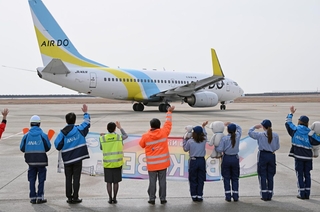 開港記念日を祝う横断幕を掲げて乗客らに手を振る航空会社の社員ら＝１６日午前、神戸空港（撮影・風斗雅博）