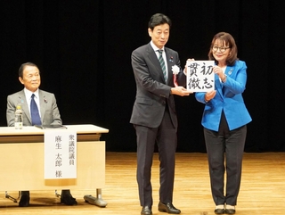 来賓の丸谷聡子明石市長（右）から色紙を受け取る西村康稔元経済産業相と、笑顔を見せる麻生太郎・自民党最高顧問＝４日午後、明石市中崎１