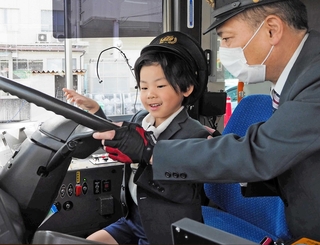 制服と帽子をかぶって、バスの運転席に座る子ども＝尼崎市東塚口町２
