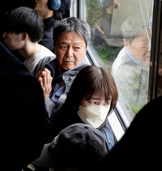 脱線事故が起きた現場付近を通過する電車内で手を合わせ、現場を見つめる乗客ら＝２５日午前９時２４分、尼崎市内（代表撮影）