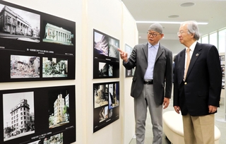 被災建物の写真と映像制作時の資料写真などが並ぶ企画展。内覧会で河田恵昭センター長（右）に三池敏夫さんが解説した＝人と防災未来センター