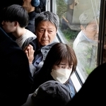 脱線事故が起きた現場付近を通過する電車内で手を合わせ、現場を見つめる乗客ら＝２５日午前９時２４分、尼崎市内（代表撮影）