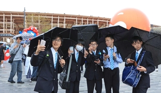 雨が降る中、傘を差して万博を楽しむ近畿大付属豊岡中の生徒たち＝大阪市此花区の夢洲