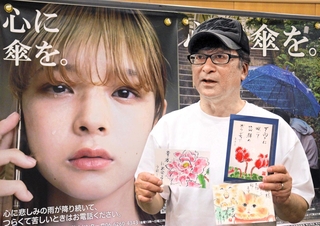 「心に傘を。」のポスターの前に立つ尾関栄二さん。これまでに支援した団体から届いた手紙を持ち、「宝物です」と話す＝三田市駅前町