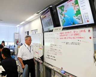 津波注意報への対応を記すホワイトボートと対応にあたる職員ら＝３０日午前１０時５８分、南あわじ市役所