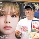 「心に傘を。」のポスターの前に立つ尾関栄二さん。これまでに支援した団体から届いた手紙を持ち、「宝物です」と話す＝三田市駅前町