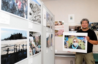 カメラマンたちが撮影した能登の写真が並ぶ京都展会場で、避難所で再会した祖母の写真を手にする頼光和弘さん＝京都府亀岡市余部町宝久保