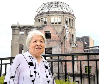 原爆ドームを背に平和への思いを語る田中洋子さん＝６日午前、広島市中区