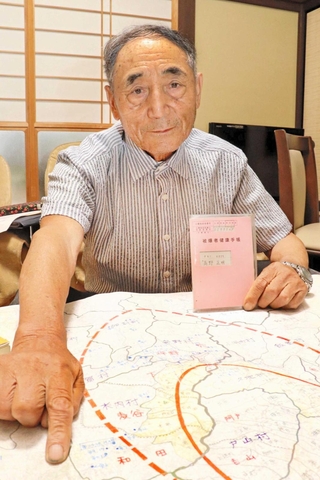 被爆者健康手帳を手に、自身が「黒い雨」を浴びた地域を指さす高野正明さん＝広島市佐伯区湯来町菅沢