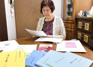 夫格知さんが残した手記を読む高橋一枝さん。手前は父横山復次さんの手記が収められていた「忘れな草」の冊子＝明石市明南町２