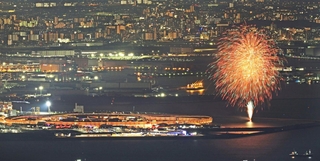 ライトアップされた大屋根リングのそばで打ち上げられる花火＝神戸市灘区六甲山町、六甲山天覧台から望む