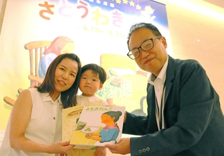 １万人目の来場者となり、記念に絵本２冊を受け取った太田三恵さん（左）と暖士君＝神戸ファッション美術館