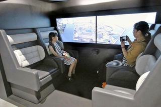 英国製の空飛ぶクルマ客室を再現した展示で、映像によるフライト体験を楽しむ親子連れ＝大阪市此花区の夢洲