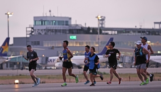 夜が明けきらない中、駐機する飛行機を背に滑走路上を走るランナーたち＝３０日朝、神戸市中央区、神戸空港