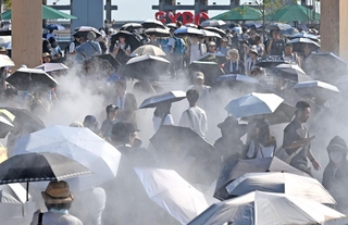 厳しい日差しが照りつける万博会場で、日傘を差しながらミストを浴びる来場者たち＝３１日午後、大阪市此花区の夢洲（撮影・大田将之）