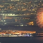 ライトアップされた大屋根リングのそばで打ち上げられる花火＝神戸市灘区六甲山町、六甲山天覧台から望む