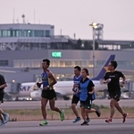 夜が明けきらない中、駐機する飛行機を背に滑走路上を走るランナーたち＝３０日朝、神戸市中央区、神戸空港