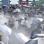 厳しい日差しが照りつける万博会場で、日傘を差しながらミストを浴びる来場者たち＝３１日午後、大阪市此花区の夢洲（撮影・大田将之）