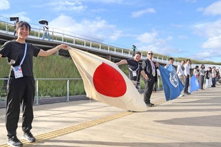 大屋根リングの上で手や旗をつなぎ、連帯を表現する各国のスタッフ＝13日朝、大阪市此花区の夢洲（撮影・岩崎昂志）