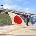 大屋根リングの上で手や旗をつなぎ、連帯を表現する各国のスタッフ＝13日朝、大阪市此花区の夢洲（撮影・岩崎昂志）