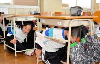 地震発生の校内放送を聞き、机の下に身を隠す児童たち＝５日午前、姫路市大塩町汐咲２